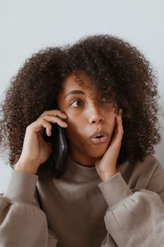 一位穿着棕色毛衣的非裔女性打电话时露出了惊讶的表情