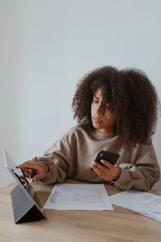 A woman using a tablet and smartphone for work at home, showcasing remote productivity.