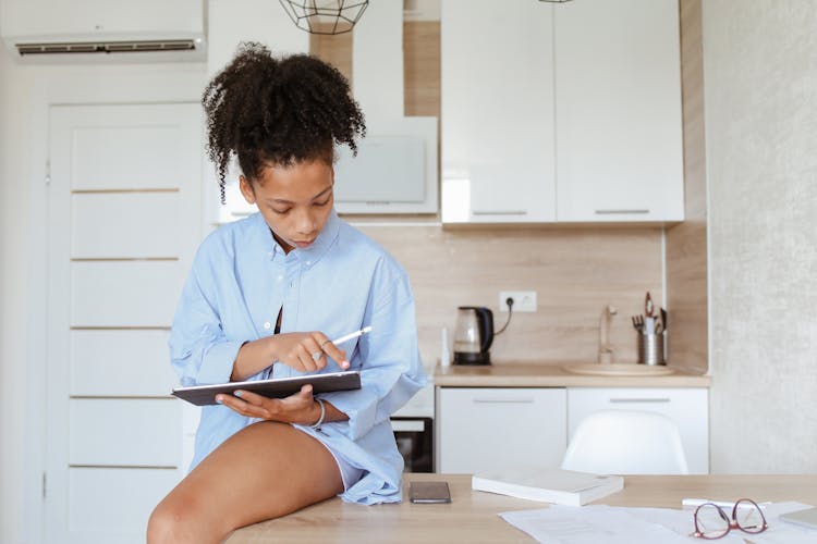 A Woman Sitting On The Kitchen Counter Using A Tablet