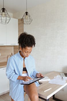 Black woman with afro hair working remotely in kitchen using a tablet.