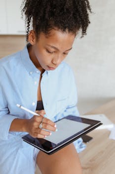 Young woman with afro hair works remotely using a stylus pen and tablet at home.