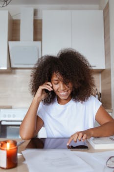 Smiling young woman using smartphone and tablet at home, representing modern remote work setup.