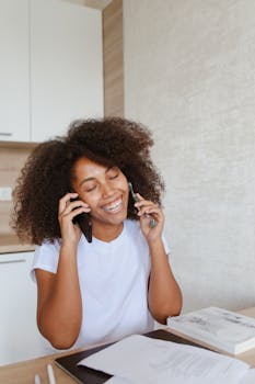 Cheerful woman with afro hair multitasking at home, working remotely and making a phone call.