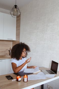 Black woman uses laptop for remote work from home kitchen.