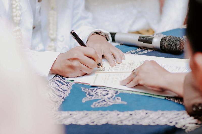 Close-up of hands signing wedding documents with microphone on table.