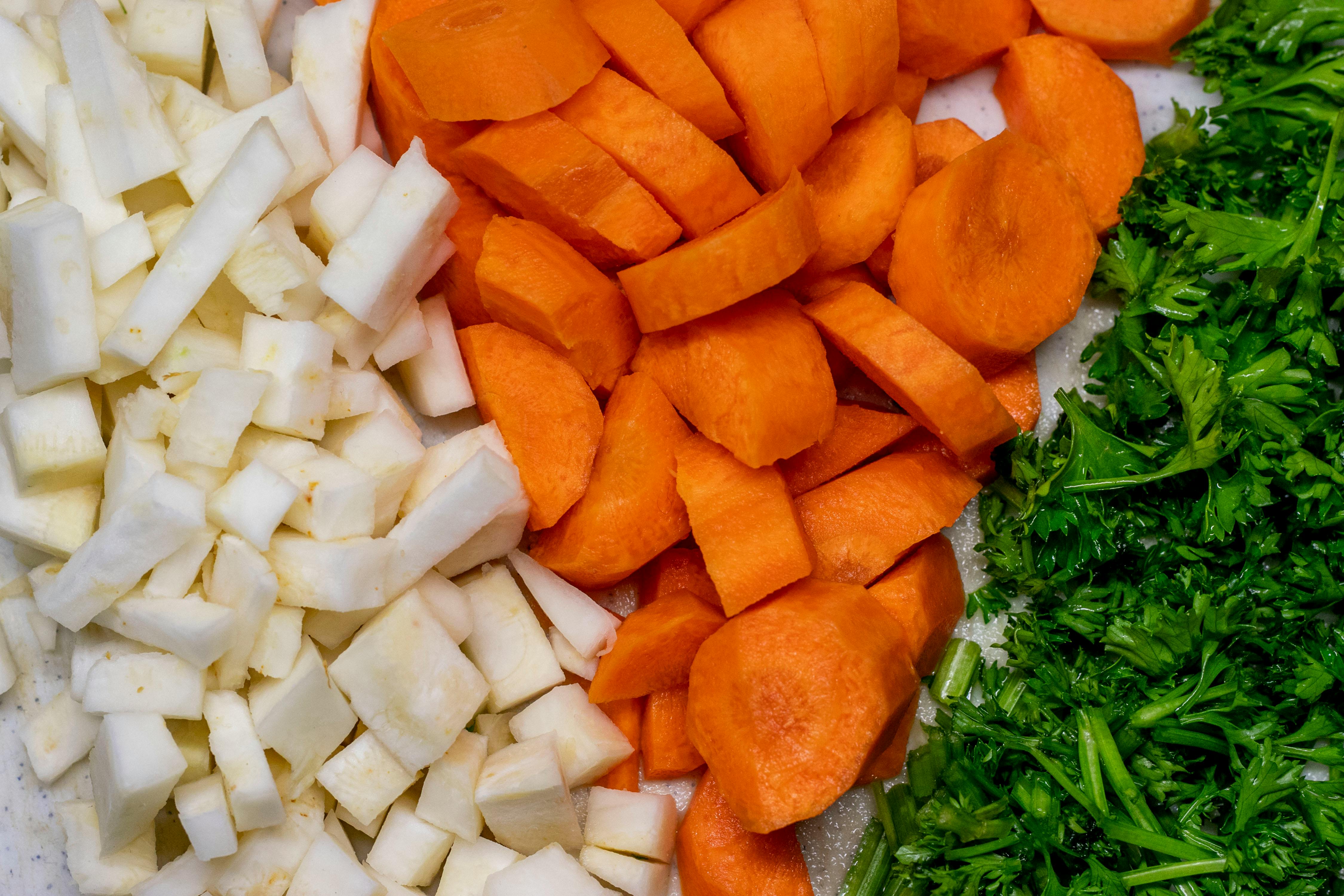 Close-up of fresh chopped carrots, parsnips, and parsley on a cutting board.