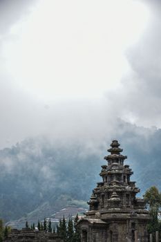 Majestic stone temple set against a misty mountain backdrop under an overcast sky. - Fotografer Sidoarjo