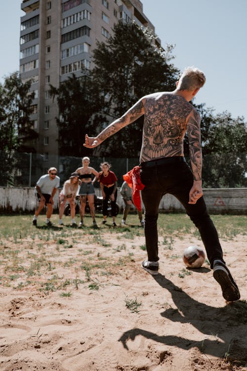 A Tattooed Man Kicking a Soccer Ball