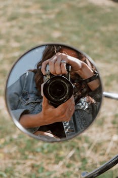 Creative shot of a woman photographing through a rearview mirror outdoors.