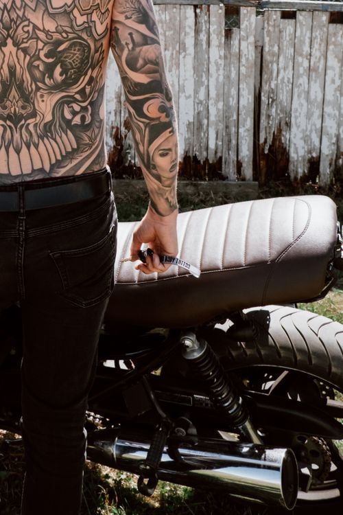 Free Shirtless tattooed biker standing next to a motorcycle, holding a key outdoors. Stock Photo