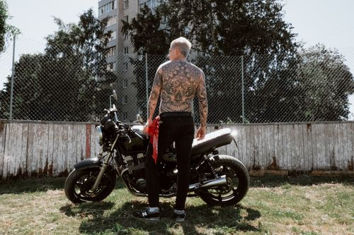 Free Shirtless tattooed man standing beside motorcycle in urban outdoor setting, exuding adventure. Stock Photo