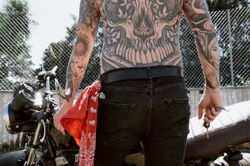 Free A Shirtless Tattoo Person Holding a Key in Front of a Motorbike Stock Photo