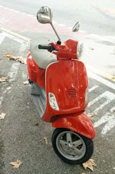 A bright red scooter parked on a street with fallen leaves, showcasing urban lifestyle.