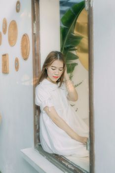 一位年轻女子身着白色连衣裙，坐在窗台旁享受宁静时光