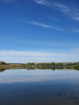 A tranquil lake in Ukraine reflects a clear blue sky and distant landscape, creating a peaceful scene.
