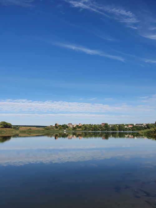 Free A tranquil lake in Ukraine reflects a clear blue sky and distant landscape, creating a peaceful scene. Stock Photo
