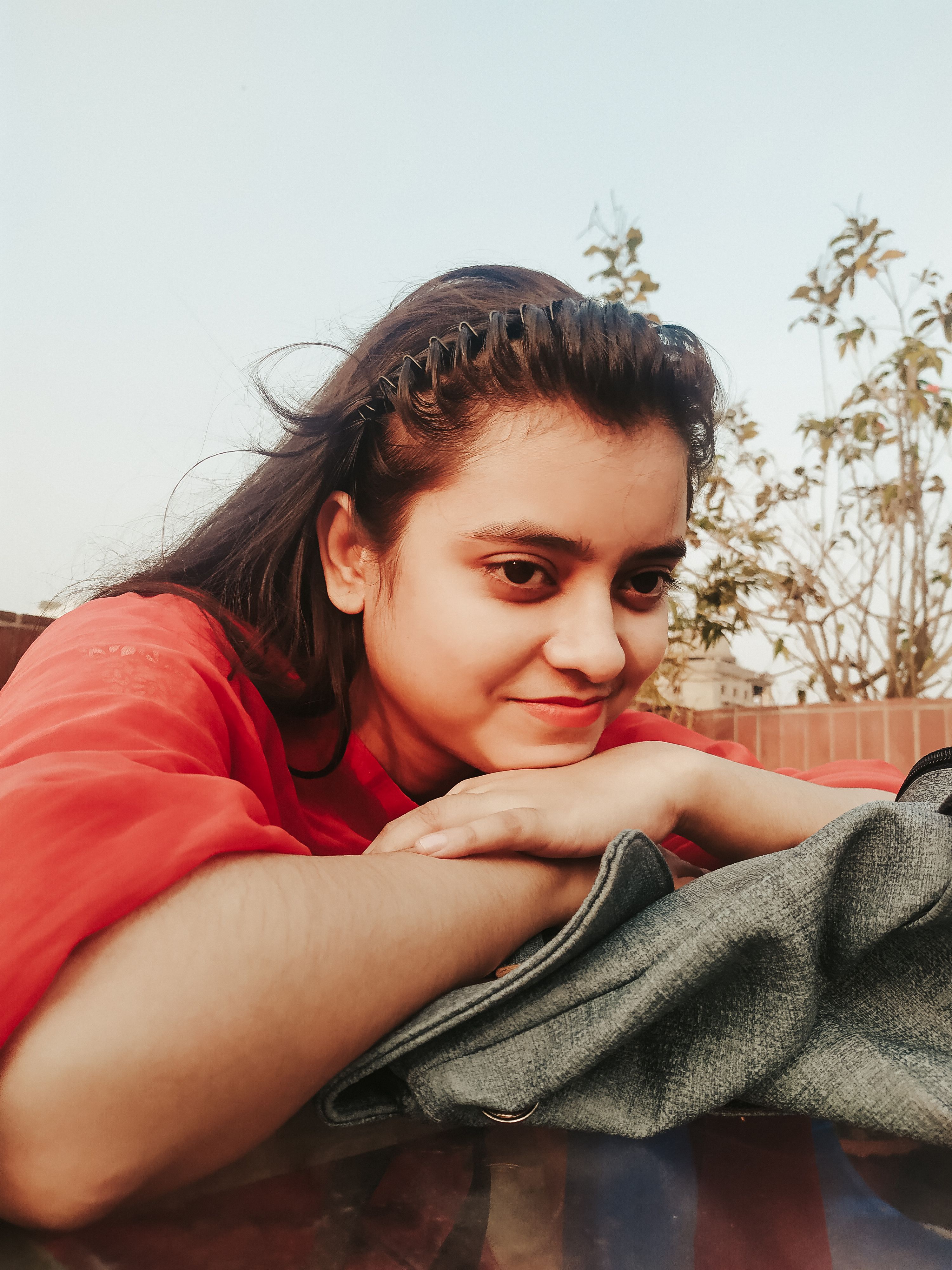 A cheerful woman in a red shirt relaxes outdoors, enjoying the warm day.