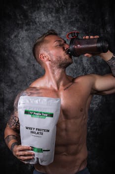 Shirtless man drinking a protein shake with whey protein bag.