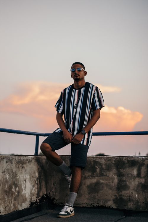 Free Full body of confident young African American male in trendy outfit and sunglasses relaxing on terrace of aged building against cloudy sunset sky Stock Photo