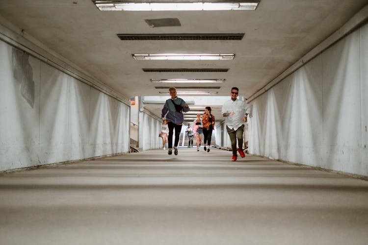 A Group Of People Happily Running In The Underground Corridor