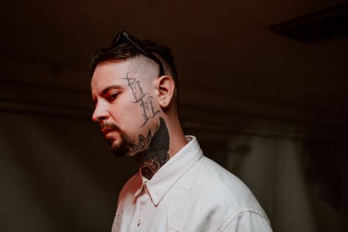 Free Close-up portrait of a tattooed man in a white shirt, captured in shallow focus indoors. Stock Photo