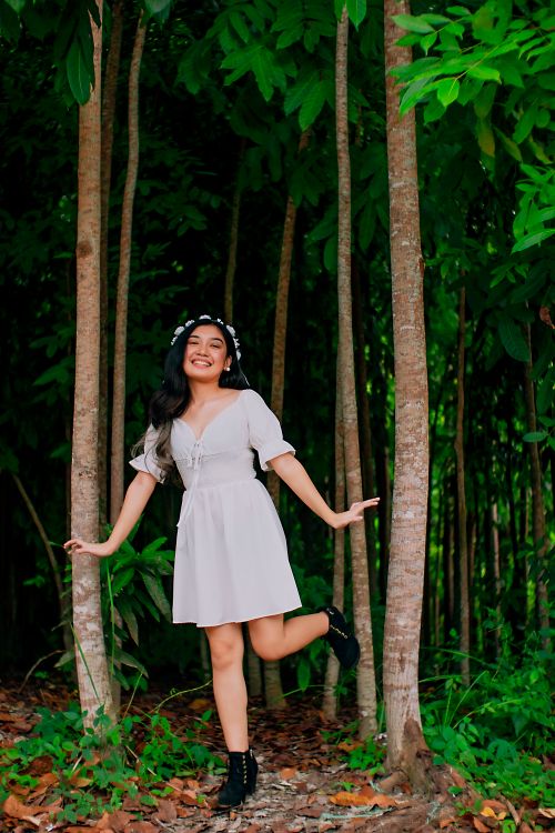 Free Happy woman in a white dress with flower crown smiling amidst trees outdoors. Stock Photo