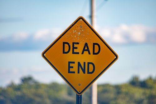 Free A close-up of a yellow 'Dead End' road sign against a scenic rural backdrop under clear skies. Stock Photo