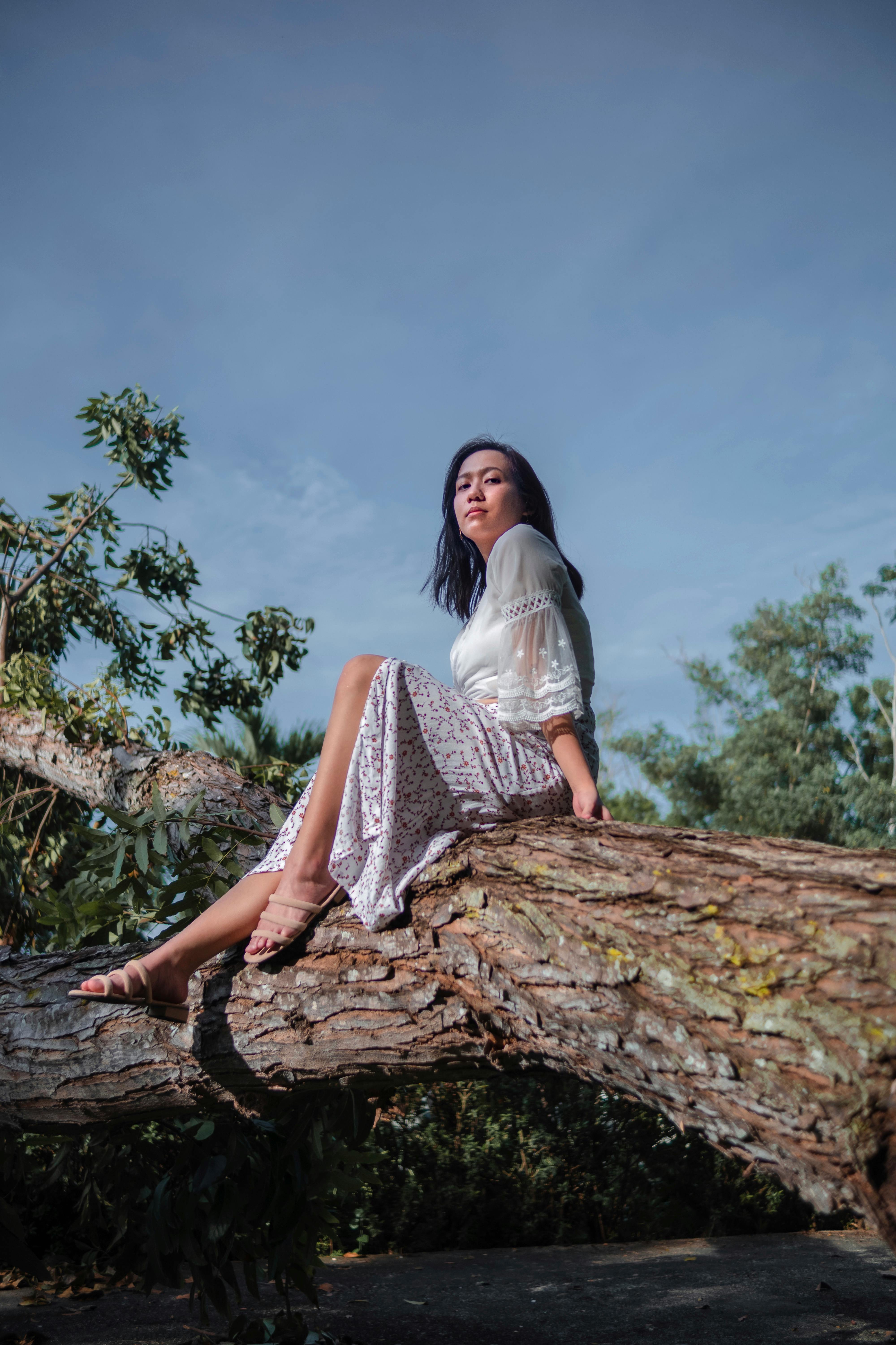 Low section of teenage girl wearing flip-flops sitting on tree trunk Stock  Photo