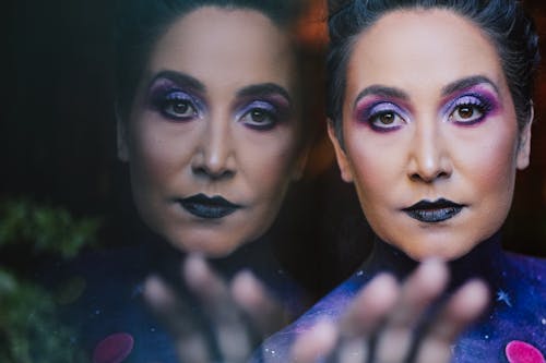 Contemplative woman with artistic makeup standing near window