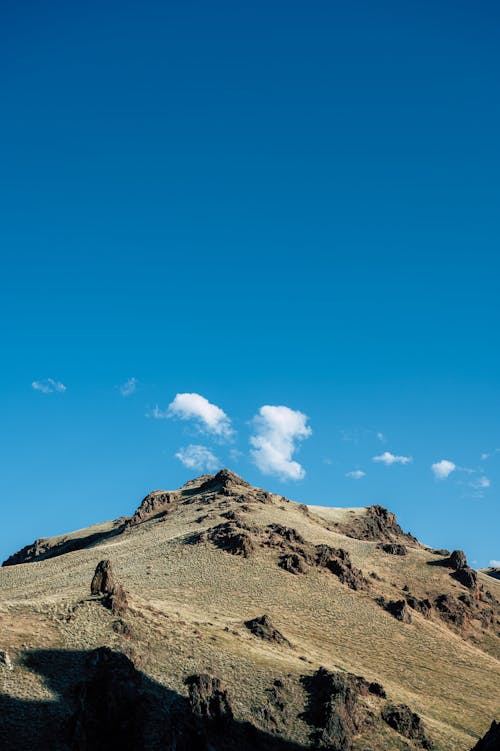 From below of picturesque mountain range with rocky formations against bright blue sky on sunny day