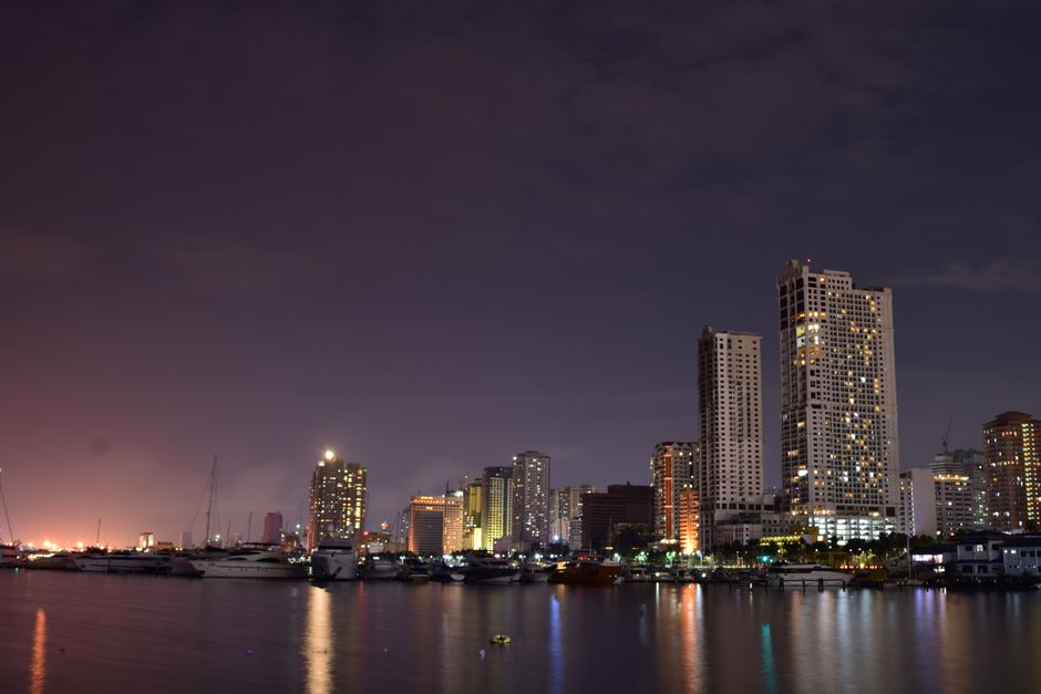 Picturesque scenery of contemporary skyscrapers located on shore of sea with moored boats against dark sundown sky in Manila