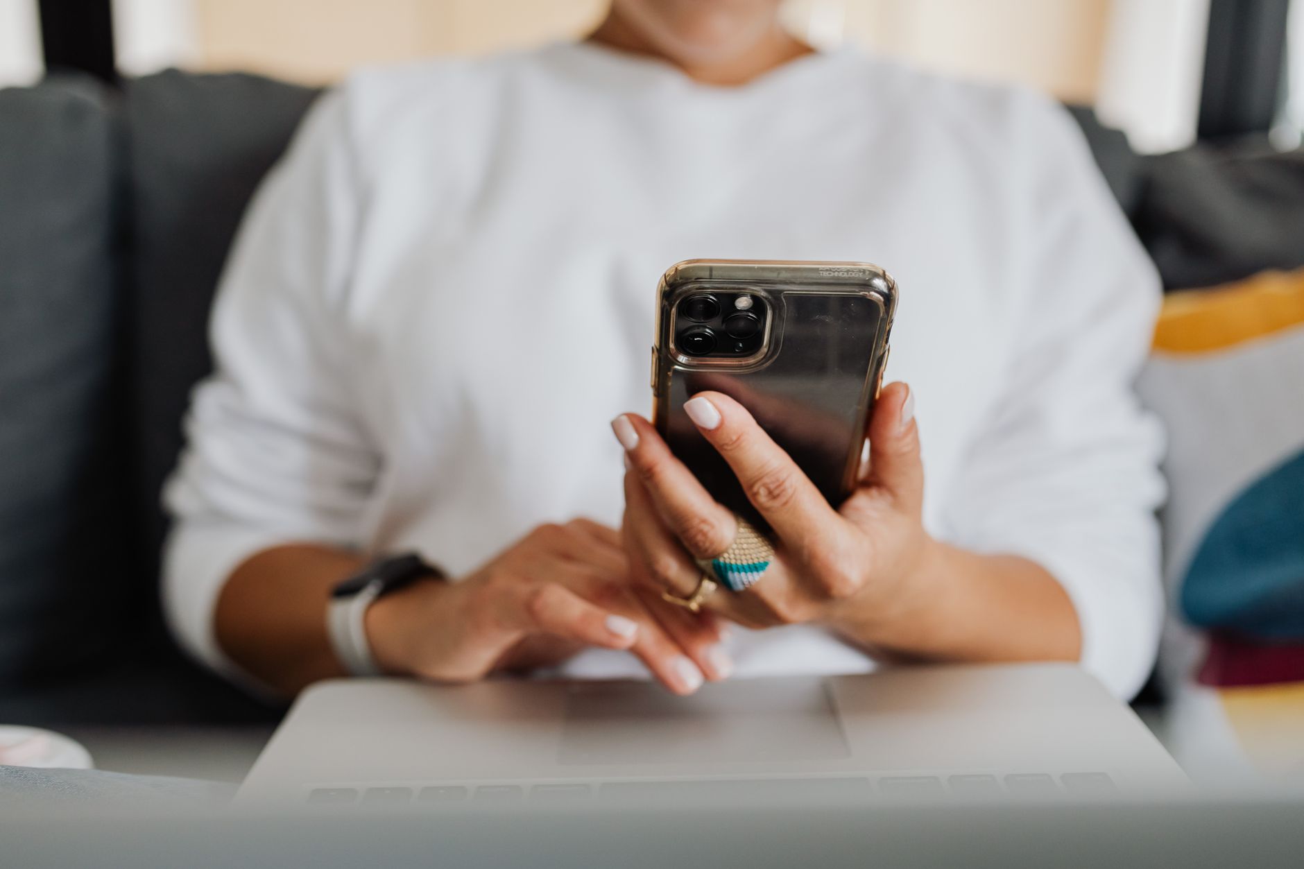 Close-up of a woman holding a smartphone and using a laptop indoors.