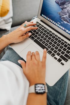 An adult typing on a laptop wearing a smartwatch, captured in a home office setting.