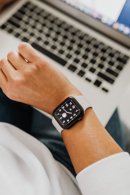 Free Close-up of a hand wearing a smartwatch positioned next to a laptop in a workspace setting. Stock Photo