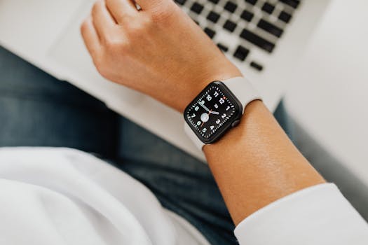 Close-up of a person wearing a smart watch while working on a laptop.