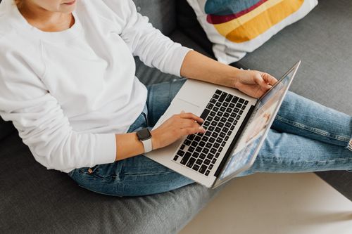 Free Person in casual attire using laptop on cozy grey sofa, creating a home workspace vibe. Stock Photo