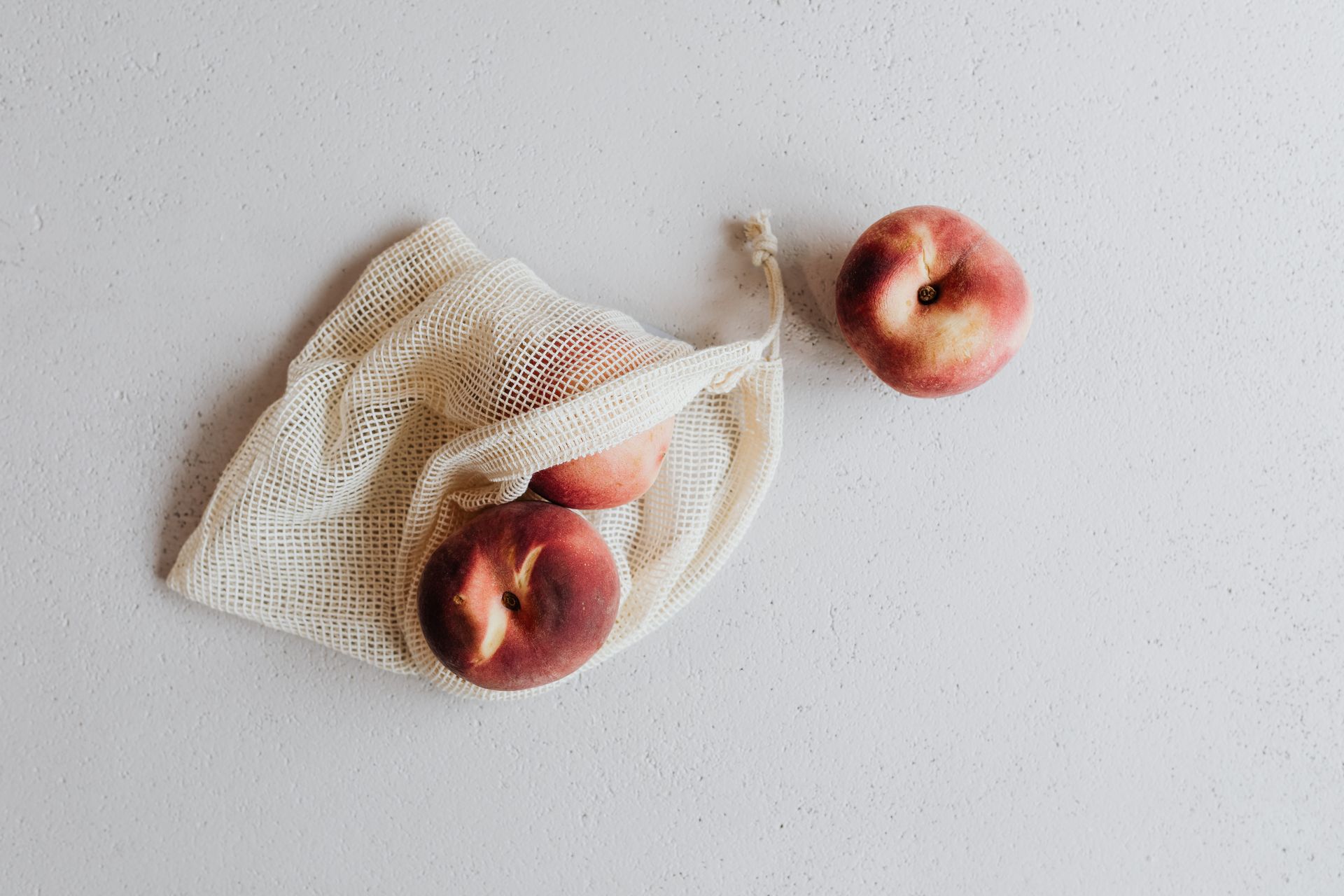 Top view of peaches in a reusable net bag on a white surface, promoting sustainability.