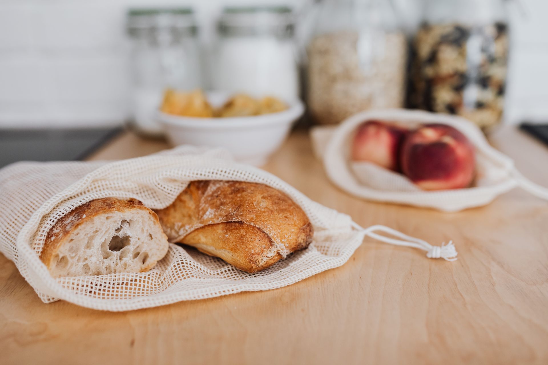 Eco-friendly kitchen scene with bread and apples in reusable mesh bags on a wooden countertop.