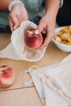Person using reusable cotton bags to store fresh peaches, promoting zero waste and sustainability.
