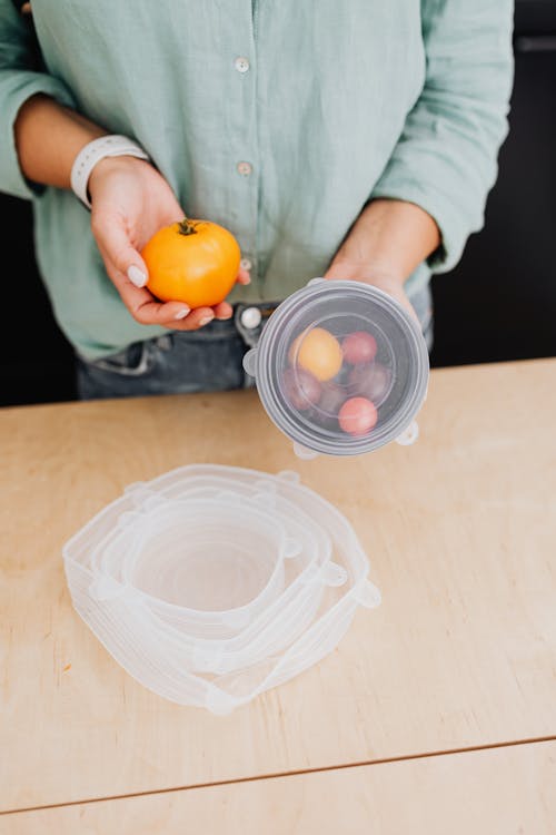 Person Holding Orange Fruit Near Clear Plastic Container