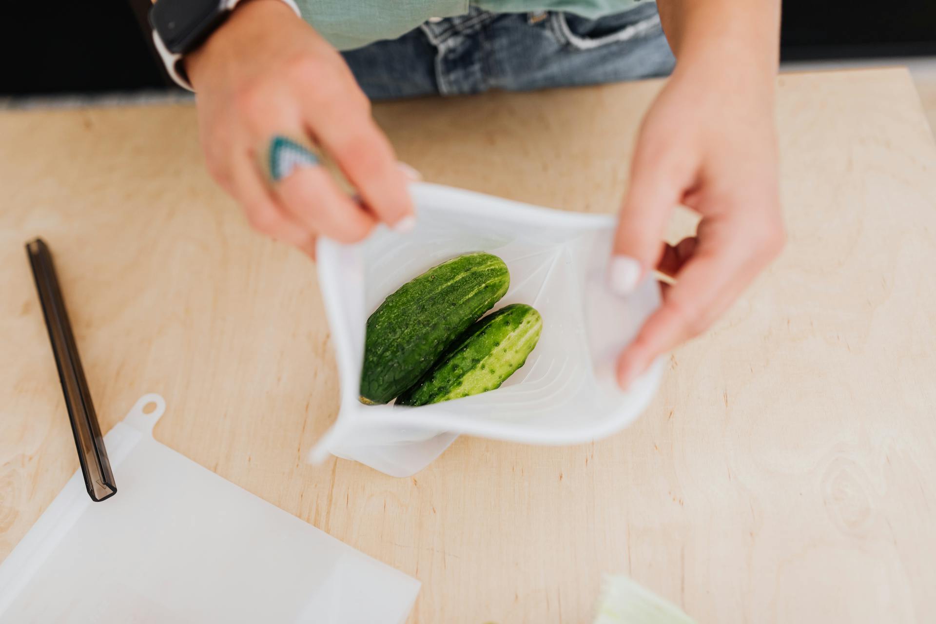 Close-up of hands placing cucumbers in a reusable pouch, promoting eco-friendly living.
