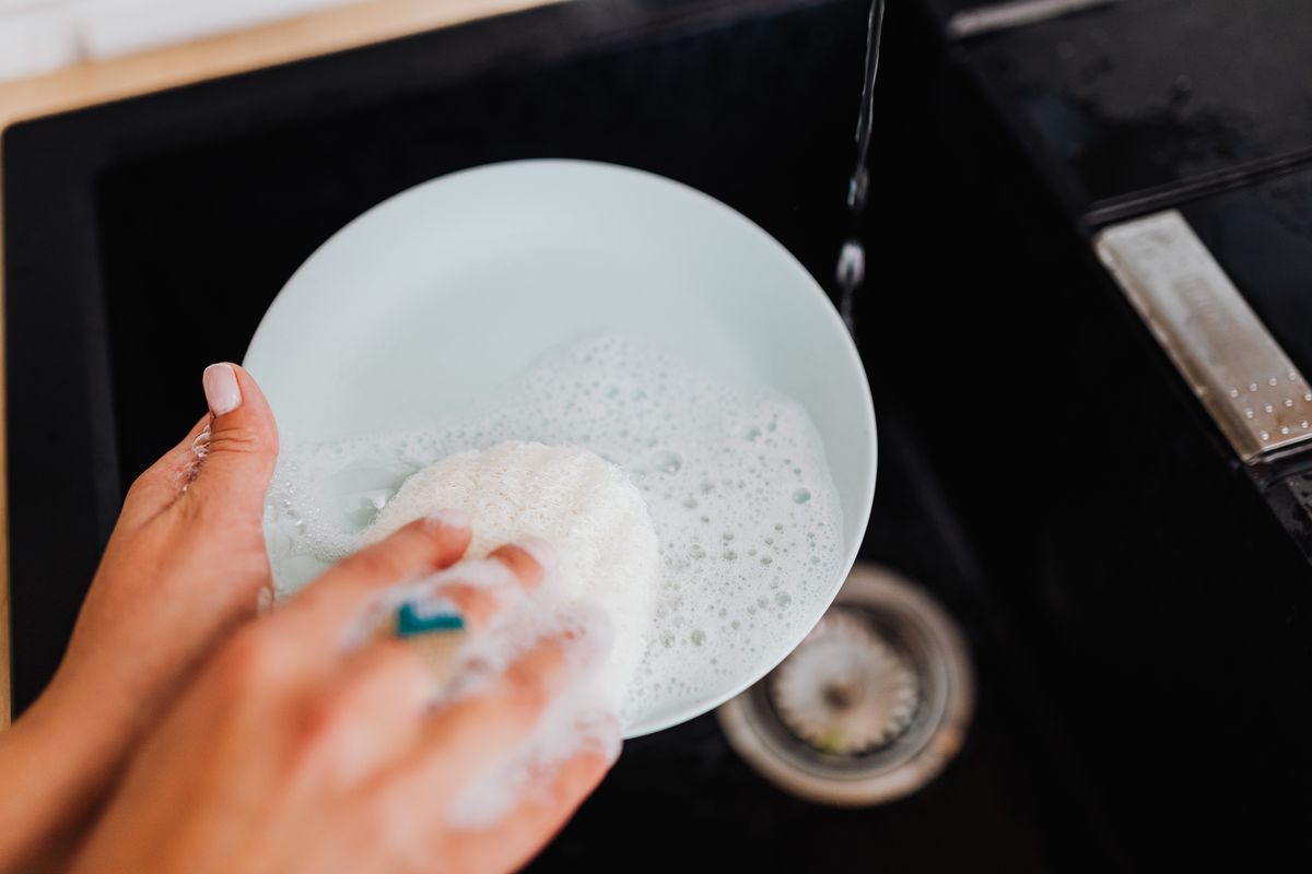 A traditional kitchen sponge generating soap suds while washing a plate at the sink