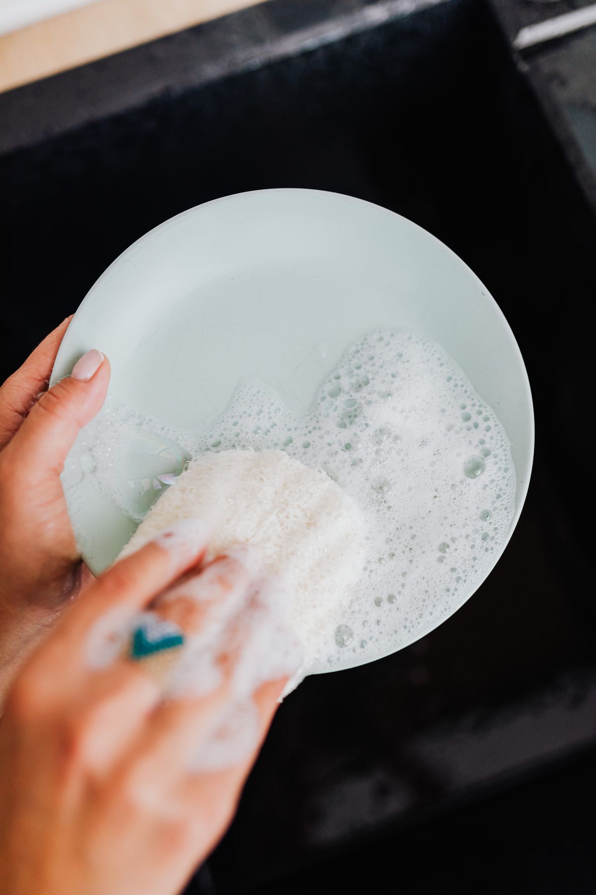 Hands washing a green plate with a sponge in a kitchen sink