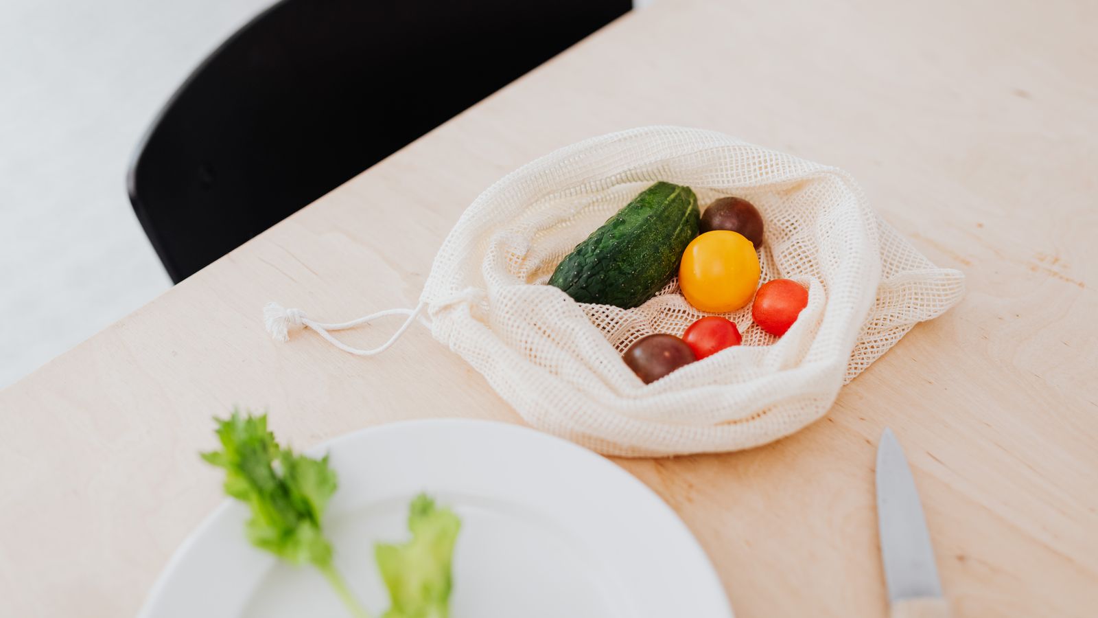 Vegetables in a mesh bag beside a plate and kitchen knife on a wooden table