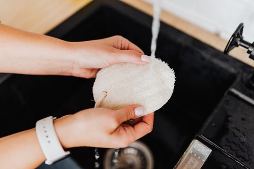 Free A woman rinses a loofah under running water in a kitchen sink. Hygiene and care concept. Stock Photo