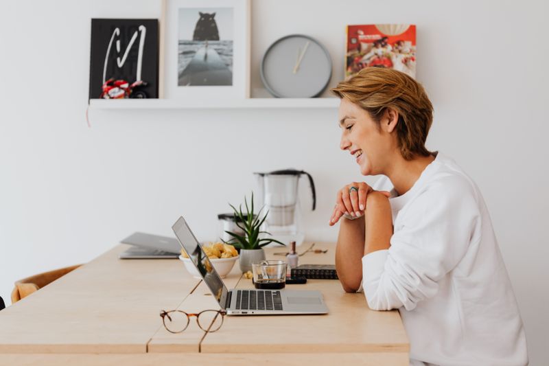 Selbstständige Frau sitzt lachend am Laptop in ihrem Homeoffice