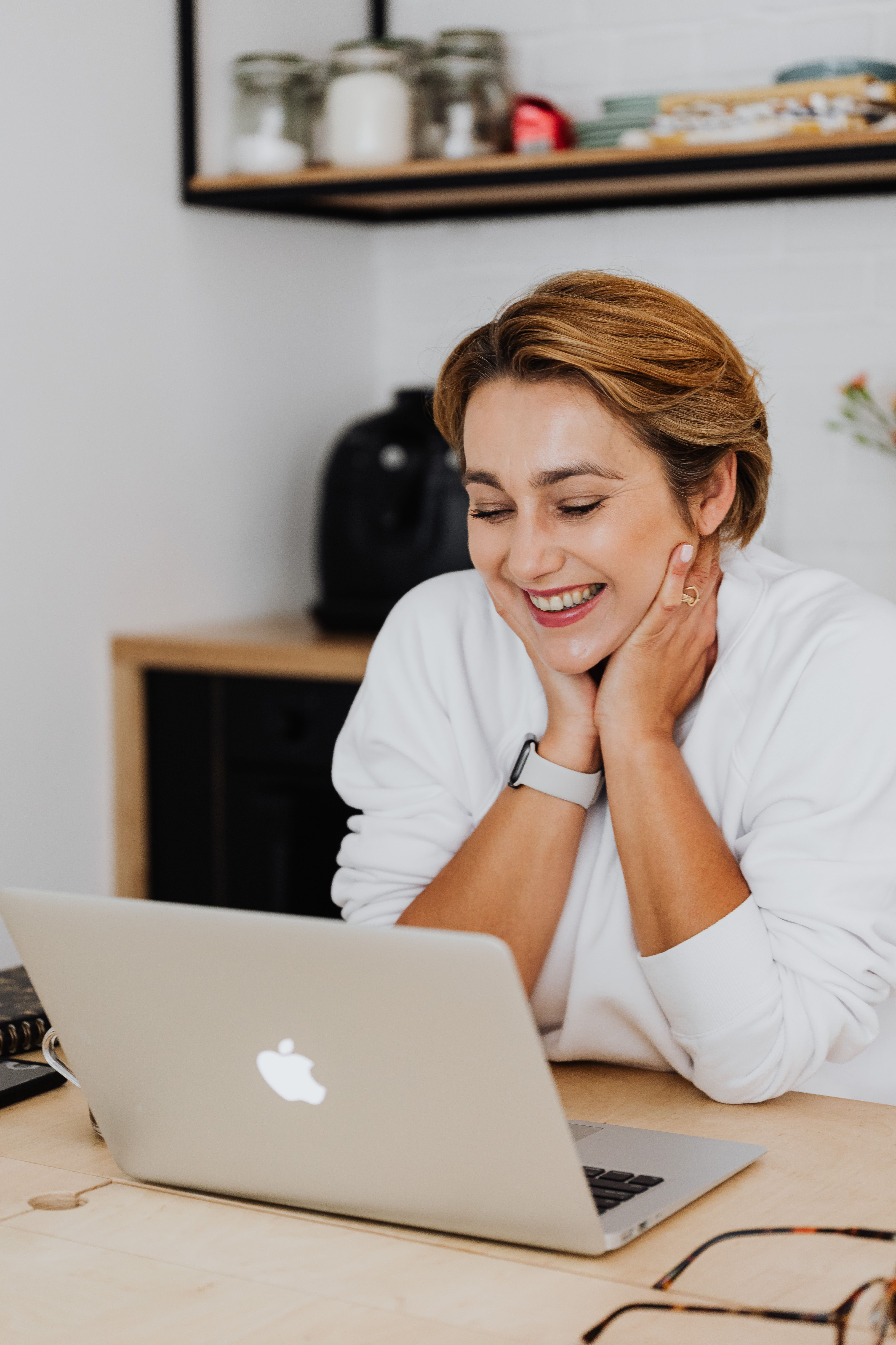 A woman smiling while using a laptop in a cozy home office setting