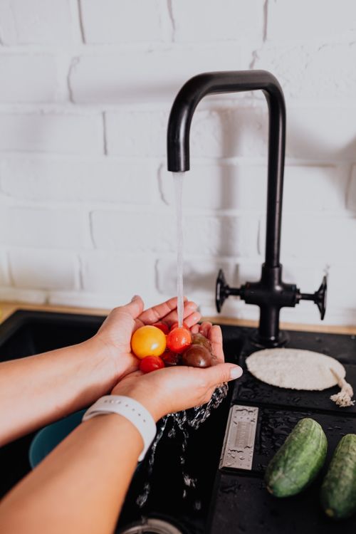 Free Close-up of woman washing cherry tomatoes under kitchen faucet. Stock Photo