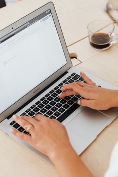 Close-up of hands typing on a MacBook Air with a coffee cup on a wooden table.