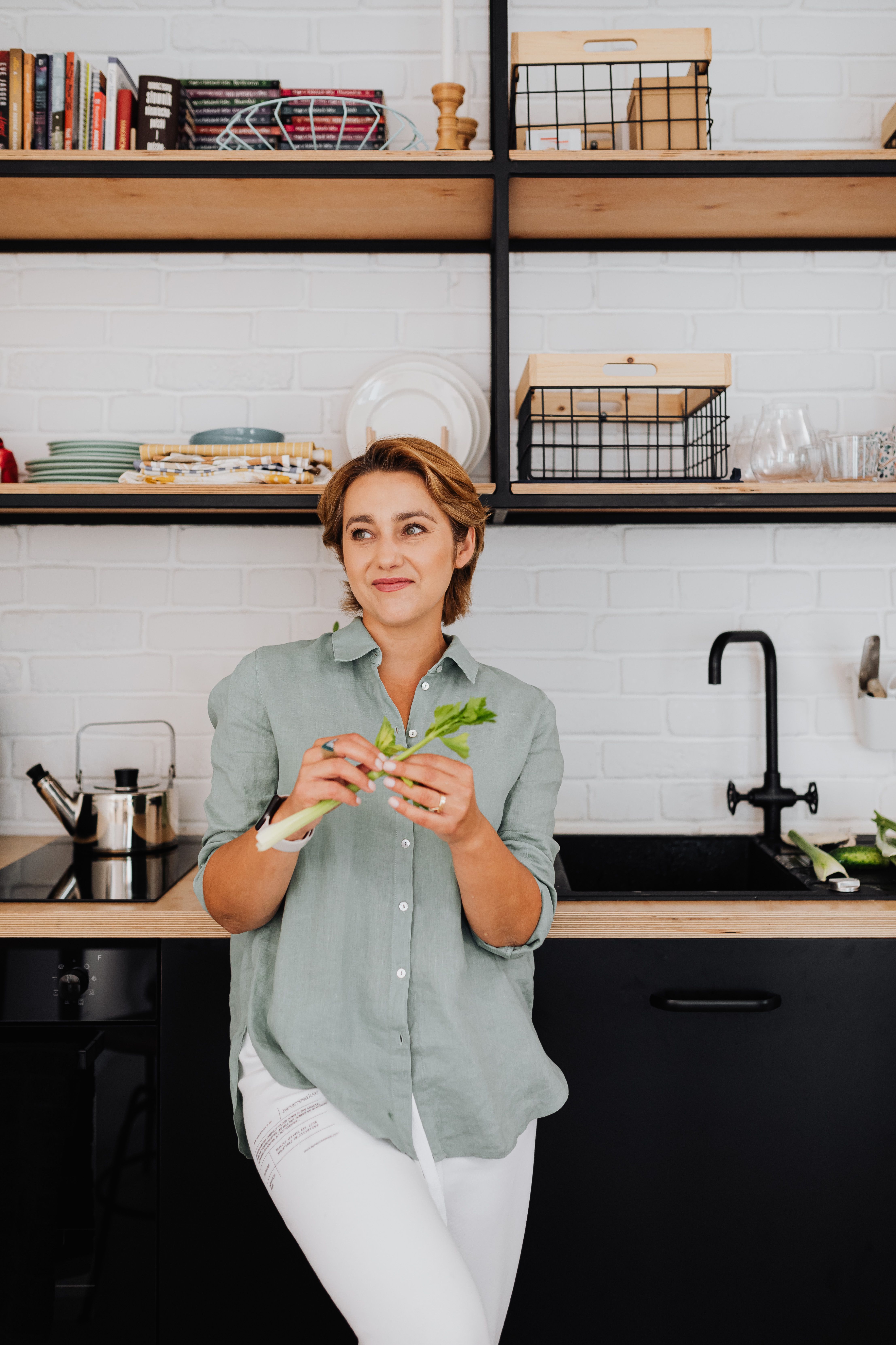 Smiling woman in a stylish kitchen preparing fresh vegetables, representing healthy lifestyle.